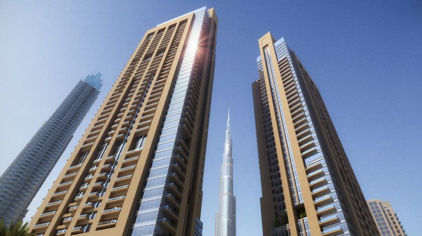 Une vue des gratte-ciels modernes de Dubaï, avec une très haute tour en arrière-plan sous un ciel bleu clair, la lumière du soleil éclairant l'un des bords du bâtiment.