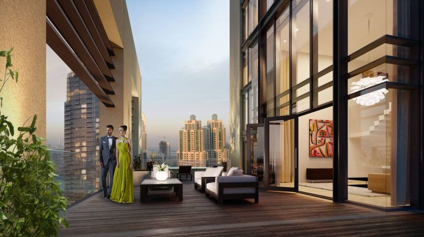 Un couple se tient sur un balcon moderne et spacieux donnant sur un paysage urbain au crépuscule, avec un mobilier d'extérieur élégant et de la verdure, à côté d'un intérieur luxueusement conçu à Blvd Heights Dubai.