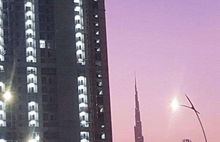 Une scène crépusculaire avec un ciel rose, mettant en vedette une grue de construction au sommet d'un immeuble de grande hauteur en construction et la silhouette du Burj Khalifa au loin à Creek Vistas, Dubaï.