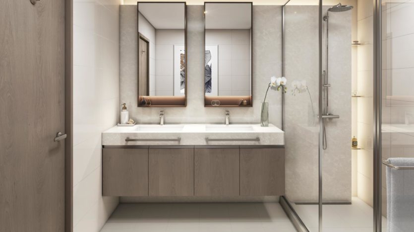 Une salle de bains moderne dotée d'une double vasque avec de grands miroirs, de meubles sous l'évier et d'un espace douche aux parois de verre. Les tons neutres et les lignes épurées dominent le design chez Elie Saab Emaar