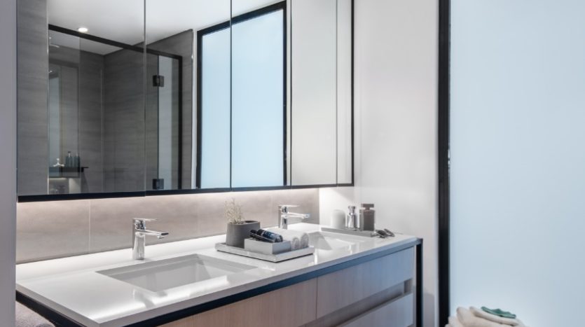 Une salle de bains moderne à Wilton Park comprenant un grand miroir au-dessus d'un meuble-lavabo à double lavabo avec rangement sous l'armoire. Les tons neutres avec des cadres noirs contrastés sont évidents, mettant en valeur un design minimaliste avec un éclairage lumineux.