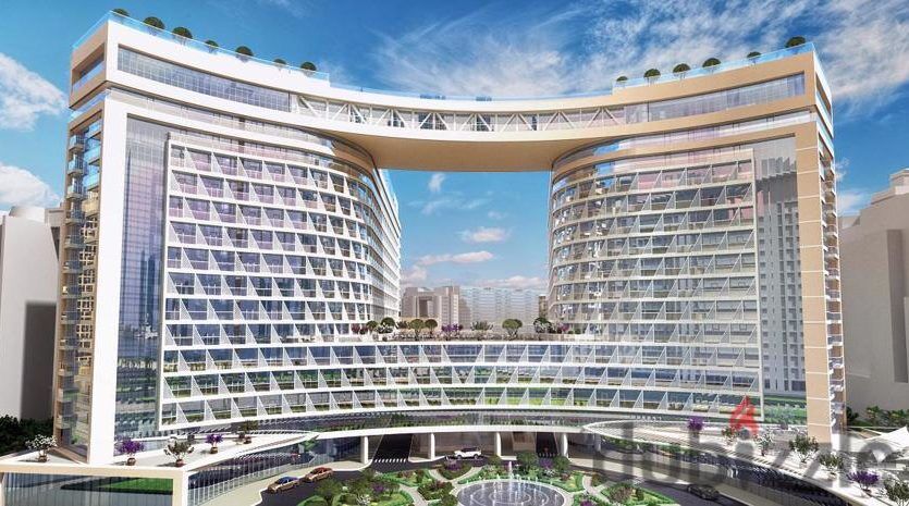 Un bâtiment futuriste à deux tours relié par un pont aérien, doté de façades en verre incurvées et de terrasses vertes, sur un ciel bleu avec des nuages épars à Seven Palm.