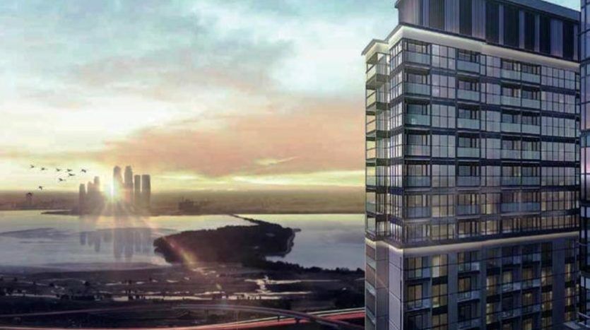 Un immeuble moderne de grande hauteur surplombe un paysage urbain pittoresque avec un coucher de soleil radieux se reflétant sur une crique et des gratte-ciel lointains à Dubaï, tandis que les oiseaux volent dans le ciel.