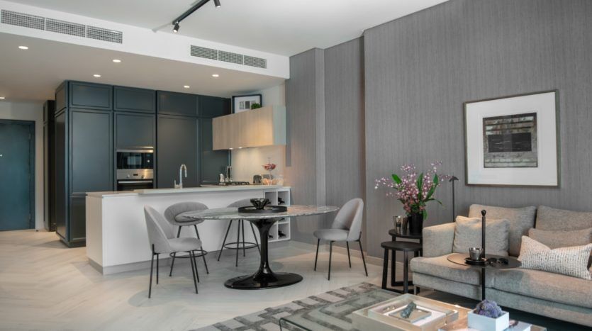 Intérieur d'appartement moderne sur le thème gris de Wilton Park, comprenant une cuisine avec des armoires bleu marine, un coin repas avec une table ronde et un espace de vie avec un canapé et un tapis. Les fleurs ajoutent une touche de couleur