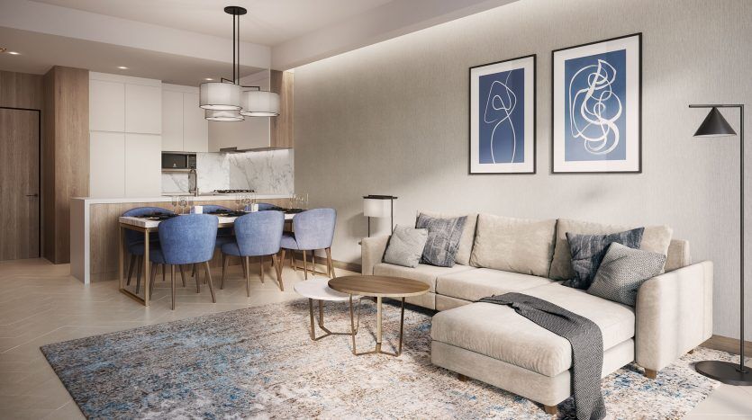 Salon moderne avec canapé sectionnel, tapis coloré et coin repas adjacent doté de chaises bleues et d'un îlot de cuisine en marbre à l'Address Residences Dubai Opera. Trois suspensions sont suspendues au-dessus.