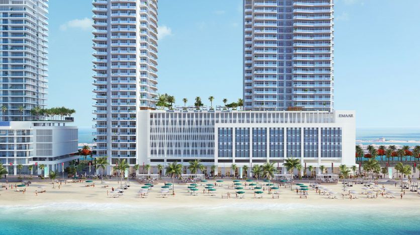 Un complexe luxueux avec vue sur la marina avec trois grands bâtiments, des palmiers, une plage de sable bondée avec des parasols colorés et un ciel bleu clair.