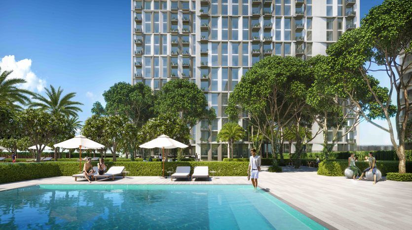 Une vue panoramique sur la piscine d'un hôtel de luxe avec des clients se relaxant sur des chaises longues, entourés d'une verdure luxuriante et le bâtiment moderne Collective 2.0 Dubai Hills en arrière-plan.