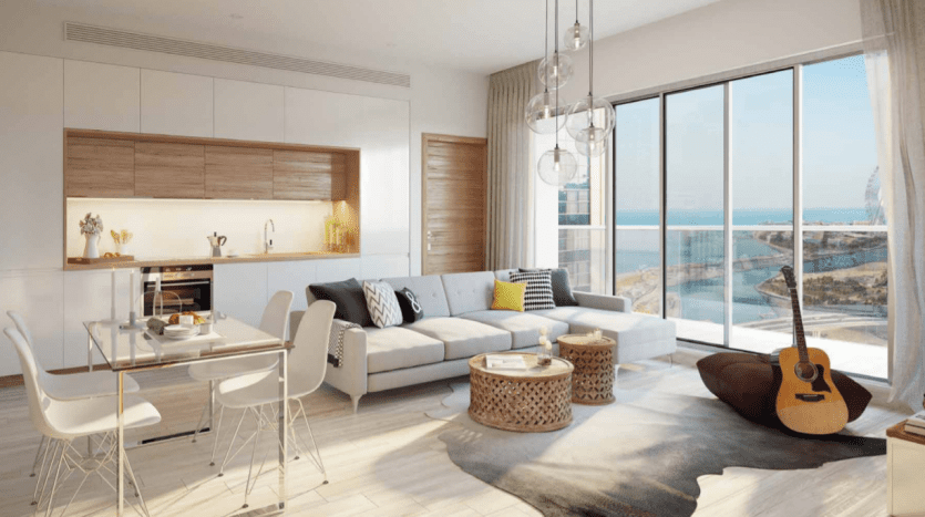 Intérieur d'un studio moderne dans la marina de Dubaï avec un plan ouvert comprenant un salon avec canapé et guitare, un espace salle à manger et une cuisine, le tout donnant sur l'océan à travers de grandes fenêtres en verre.