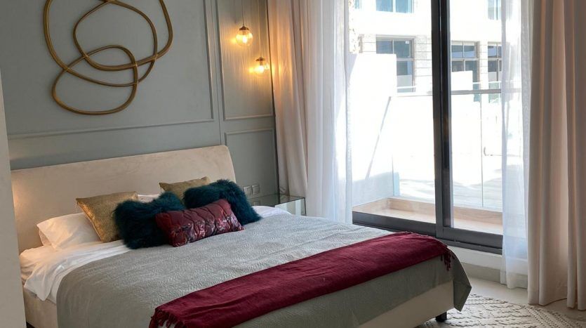 Une chambre moderne au design minimaliste avec un lit gris, des draps blancs, des coussins colorés, des murs bleu clair et une œuvre d'art murale unique. La pièce dispose de grandes fenêtres offrant une vue imprenable sur