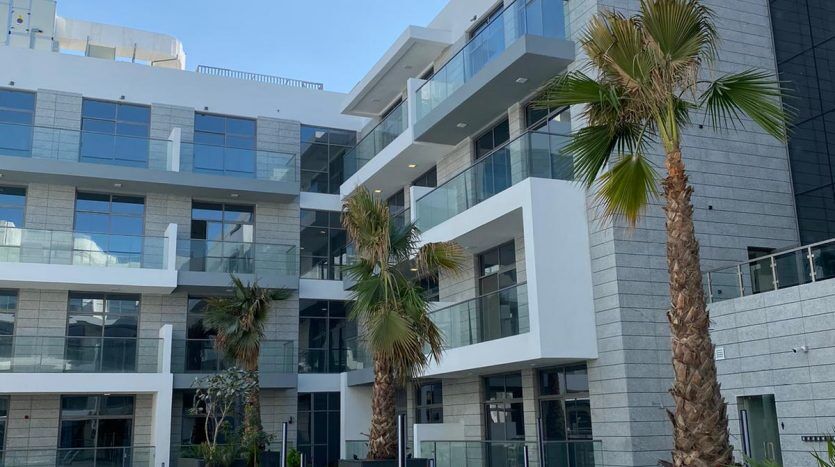 Immeuble d'appartements moderne à l'architecture blanche à Dubaï, doté d'une pelouse avec des chaises longues, des palmiers et des allées vertes rayées sous un ciel bleu clair.