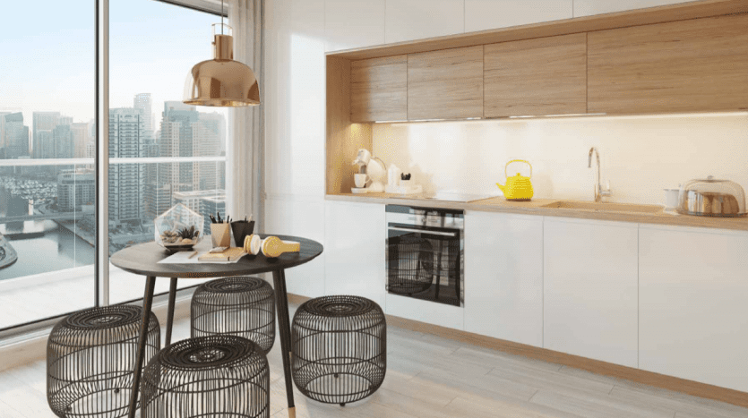 Cuisine moderne avec armoires en bois élégantes, appareils électroménagers intégrés et coin repas avec d'élégantes chaises en fil noir. De grandes fenêtres offrent une vue sur le paysage urbain dense autour du Studio One Dubai Marina. Lumineux et aéré