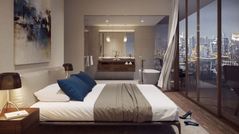 Chambre moderne du Jumeirah Living Marina Gate avec un grand lit, une salle de bains attenante et des baies vitrées donnant sur un paysage urbain la nuit. Décoration intérieure élégante avec un éclairage subtil.