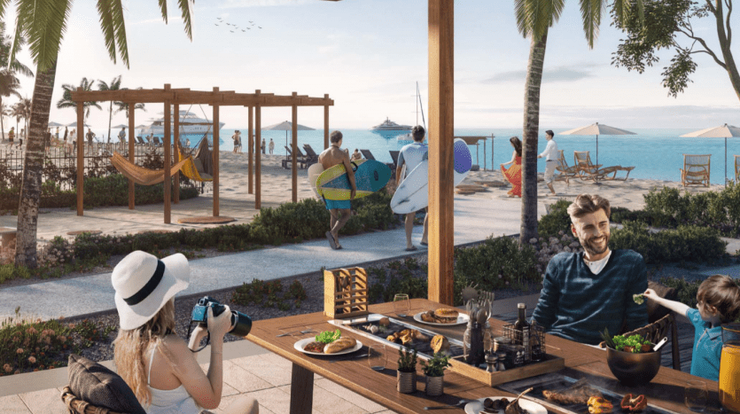 Une station balnéaire animée à La Voile, Port de la Mer, avec des gens qui dînent, marchent et se détendent au bord du rivage. Certains surfent, s'allongent dans des hamacs et prennent leurs repas en plein air