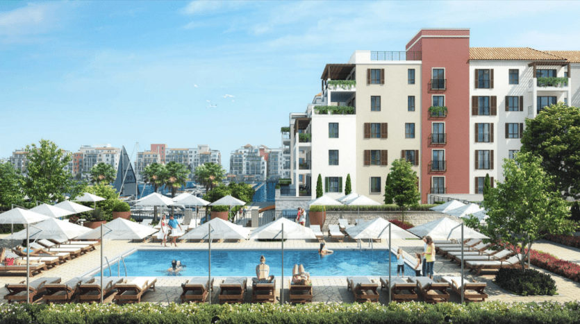 Quartier résidentiel de luxe à La Voile Port de la Mer avec une piscine extérieure étincelante entourée de chaises longues et de parasols, flanquée de bâtiments modernes à plusieurs étages et d'une verdure luxuriante sur un terrain ensoleillé.