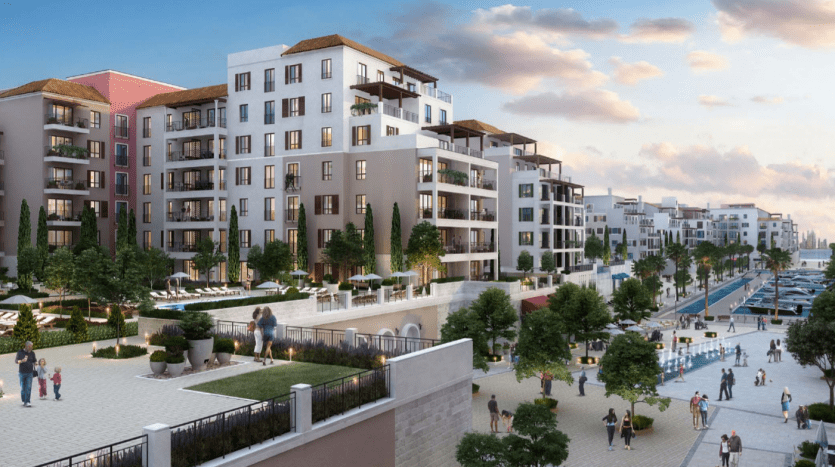Une vue panoramique de La Voile Port de la Mer avec des immeubles d'appartements modernes, une promenade animée avec des passants et des bateaux amarrés le long d'une marina sous un ciel clair au crépuscule.