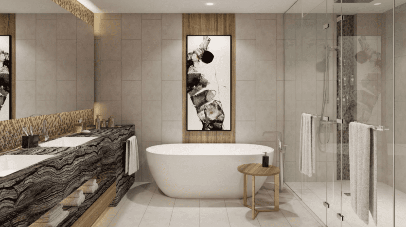 Intérieur de salle de bains moderne du Jumeirah Living Marina Gate comprenant une baignoire autoportante blanche, deux lavabos avec comptoirs texturés, des œuvres d'art murales artistiques en noir et blanc et une cabine de douche en verre transparent.
