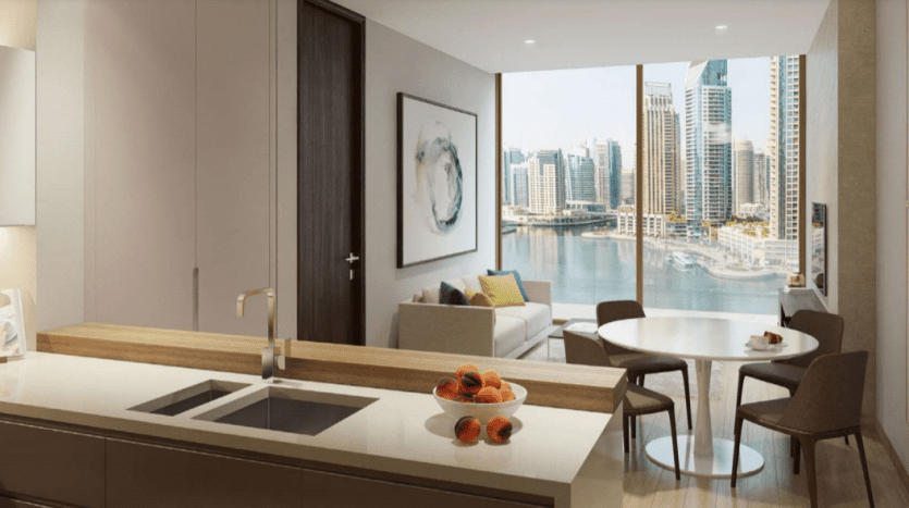 Cuisine et salon modernes donnant sur Jumeirah Living Marina Gate, avec une grande fenêtre, un bol de fruits sur le comptoir et un coin repas confortable.