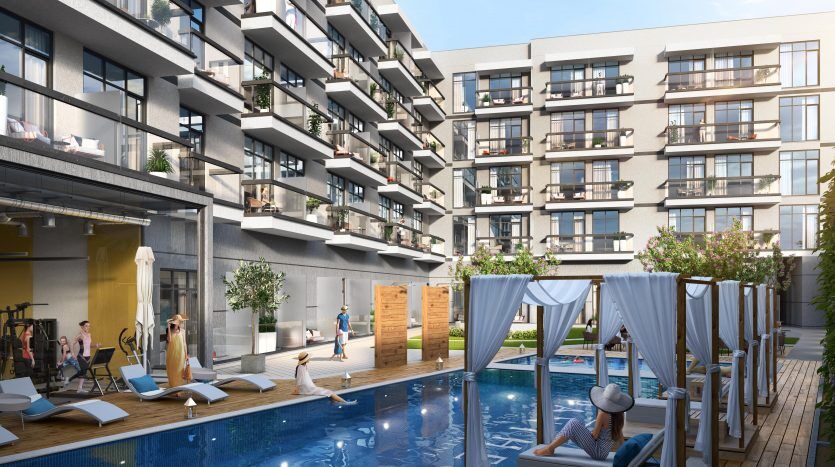 Immeubles d'appartements modernes du Panthéon Elysée 2 avec balcons donnant sur une piscine commune dotée de chaises longues, de cabanes et de résidents profitant de la journée ensoleillée.