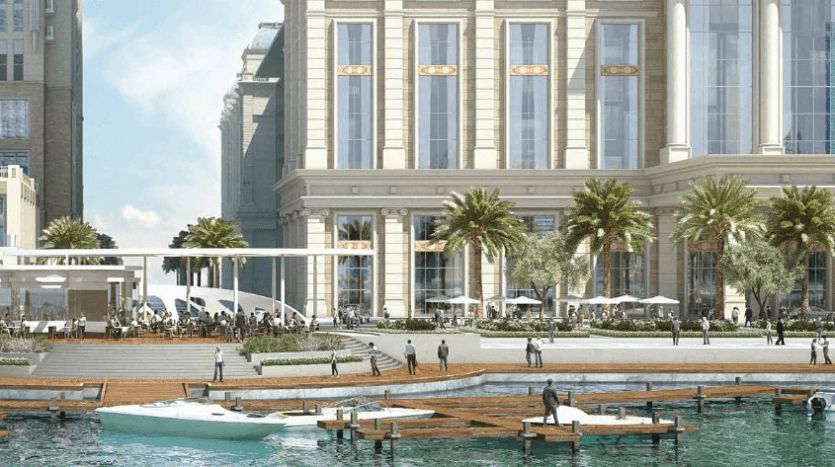 Une vue sur le front de mer avec la grande tour Amna de la ville d'Al Habtoor, flanquée de palmiers. Les gens se promènent le long de la promenade et les petits bateaux sont amarrés aux quais flottants.
