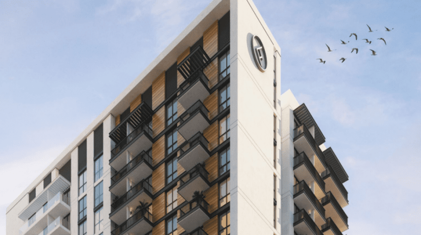 Un immeuble d'appartements moderne de grande hauteur à Sloane JVC avec une élégante façade blanche et beige, dotée de plusieurs balcons. Une volée d'oiseaux vole dans le ciel bleu à côté.