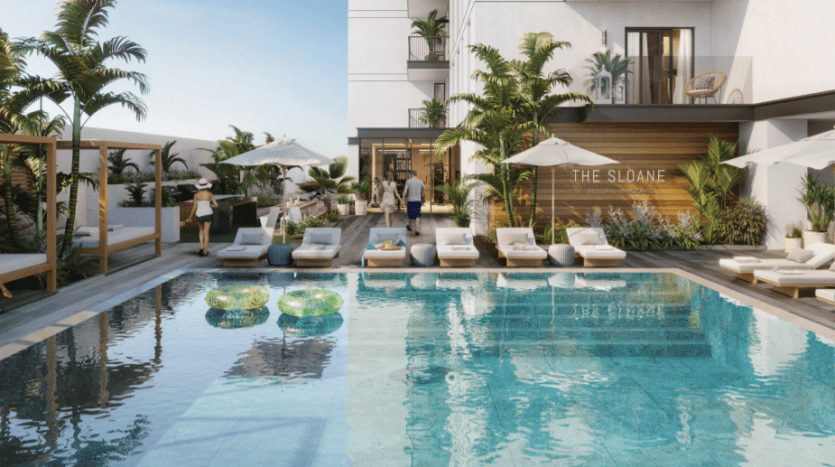 Espace piscine de luxe au "Sloane JVC" avec une eau bleu clair, entouré de chaises longues et de plantes tropicales. Les gens socialisent et profitent de la journée ensoleillée.