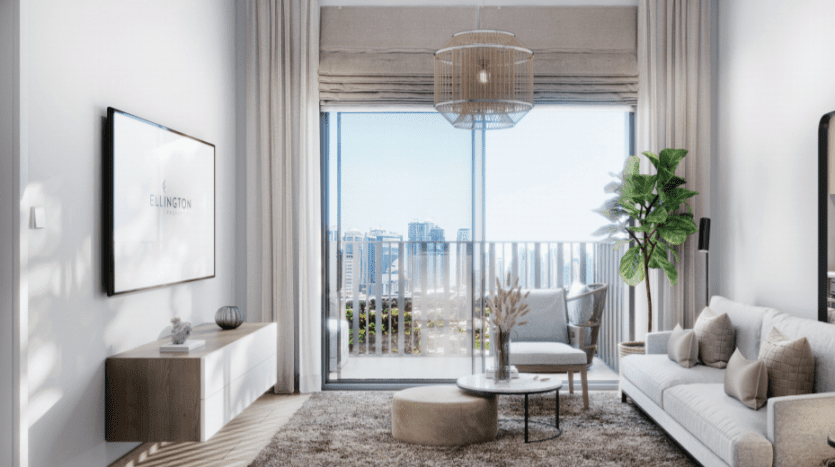 Salon moderne avec de grandes fenêtres donnant sur la ville, comprenant un canapé Sloane beige, une table basse ronde, une plante en pot et une télévision murale. La lumière du soleil brille, créant un