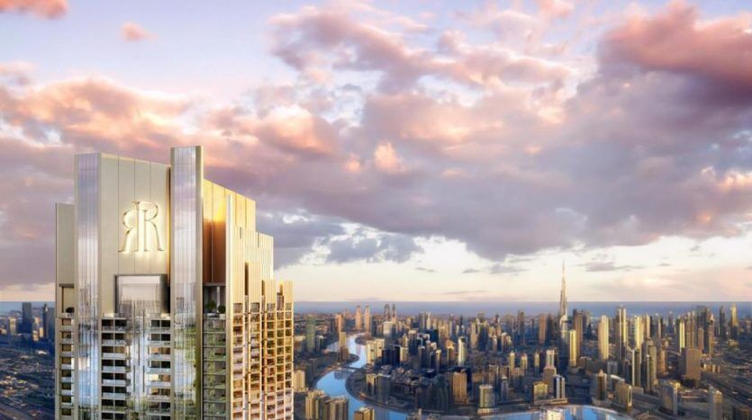 Un rendu numérique d'un luxueux immeuble de grande hauteur avec la lettre « r » au sommet, surplombant un paysage urbain tentaculaire traversé par une rivière au coucher du soleil à Dubaï.
