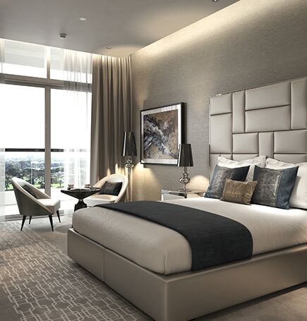 Une chambre moderne à Kiara Damas Hills, comprenant un grand lit avec des oreillers moelleux, une tête de lit rembourrée, des lampes élégantes et un coin salon près de la fenêtre, le tout dans une palette de couleurs neutres