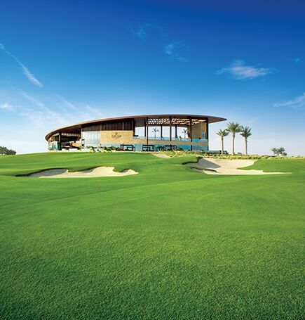Un club-house moderne avec un grand toit incurvé surplombe le parcours de golf immaculé de Kiara Damans Hills, avec des greens bien entretenus, des bunkers de sable et des palmiers dispersés sous un ciel bleu clair.