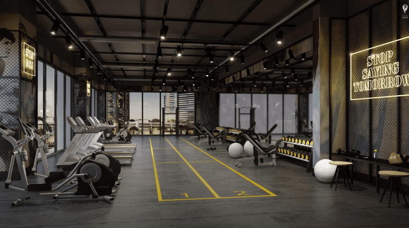 Un intérieur de salle de sport spacieux et moderne comprenant des tapis roulants, des équipements de musculation, une piste de sprint avec des voies numérotées et de grandes fenêtres offrant une vue sur la ville. Une enseigne au néon indique "Arrêtez de dire demain". Dirigé par