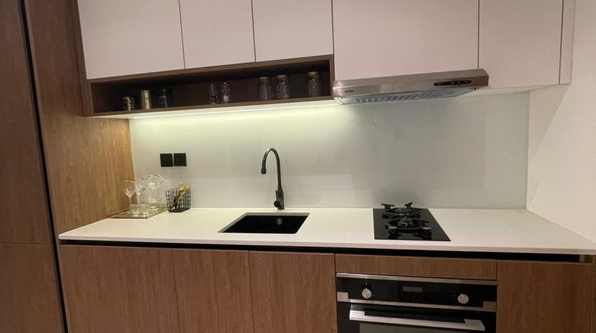 Une cuisine moderne dans Prime Residency 3 avec des armoires blanches et en bois, des appareils électroménagers intégrés en acier inoxydable et un comptoir noir. La cuisine comprend un évier, une cuisinière, un four et une hotte aspirante