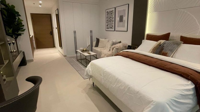 Chambre moderne dans Prime Residency 3 avec un grand lit, une literie blanche et une tête de lit sombre. Les caractéristiques comprennent une table d'appoint, des œuvres d'art sur les murs, une chaise ronde et un éclairage élégant