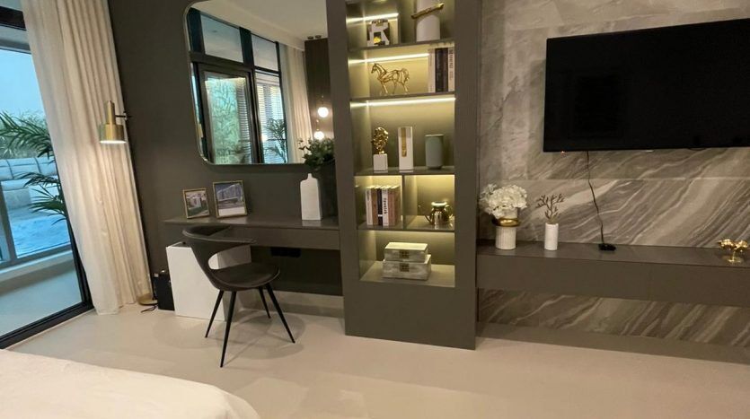 Une chambre moderne dans Prime Residency 3 avec un design élégant, comprenant un lit, une télévision murale, des détails en marbre, un bureau avec une chaise et une étagère intégrée éclairée par