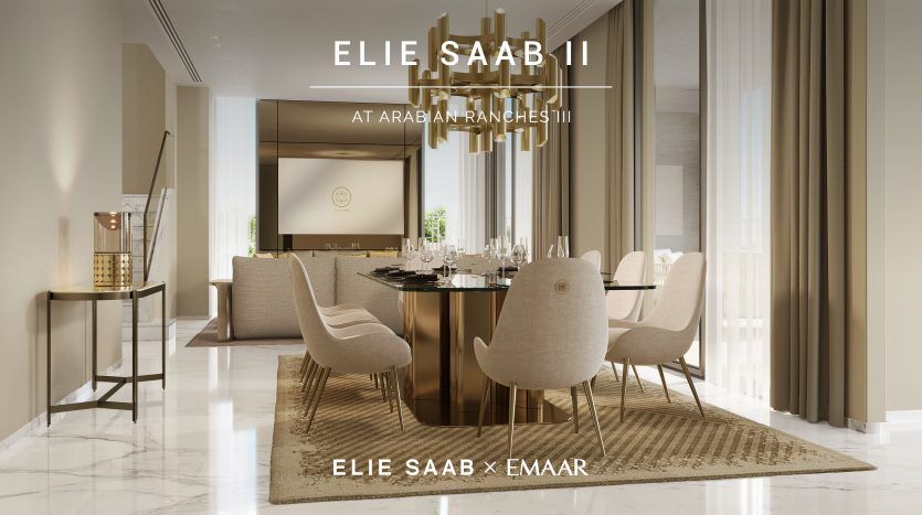 Une salle à manger luxueuse comprenant une grande table pour huit personnes, entourée d'élégantes chaises crème, sous des suspensions élégantes, avec le texte "Elie Saab at Arabian Ranches II Elie Saab