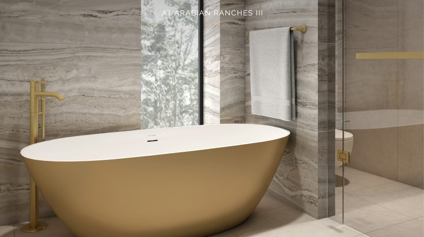 Une salle de bains luxueuse dotée d'une élégante baignoire autoportante de forme ovale au fini or mat, sur fond de murs en marbre gris élégamment veinés et d'un sol au sol conçu par Elie Saab.