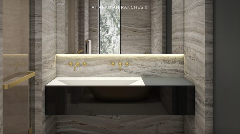 Salle de bains moderne conçue par Elie Saab Arabian Ranches, avec des murs et des sols en marbre avec un élégant lavabo blanc, sous un grand miroir encadré par une bordure noire. Accents dorés et logo "El