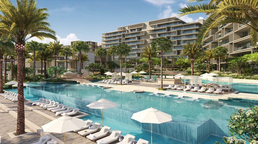 Complexe luxueux avec piscine à débordement entourée de palmiers et de chaises longues, surplombant des bâtiments modernes à plusieurs étages sous un ciel dégagé à Dubaï.