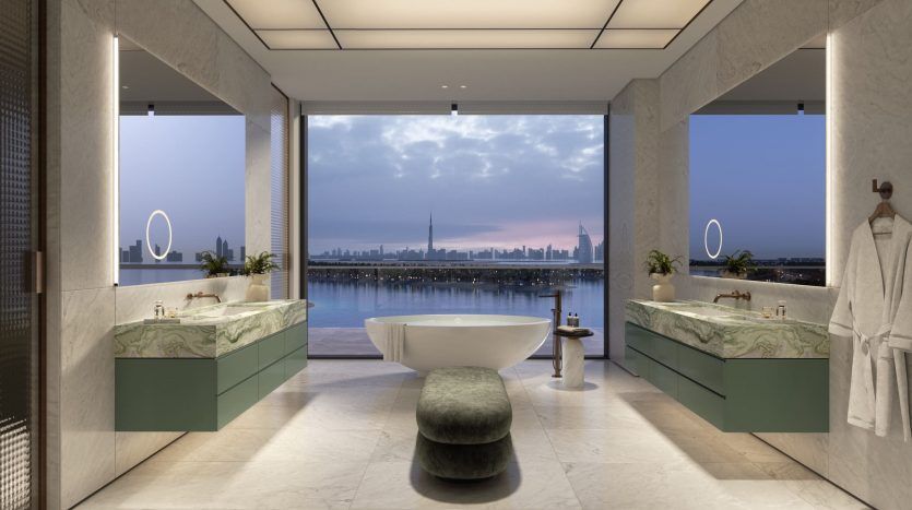 Salle de bains luxueuse avec double vasque en marbre, baignoire autoportante et baies vitrées mettant en valeur les toits de la ville au crépuscule. Des robes blanches de Six Senses sont suspendues à côté de miroirs ovales.