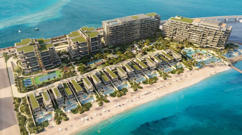 Vue aérienne d'un complexe hôtelier de luxe Six Senses en bord de mer avec des rangées de villas menant à des bâtiments à plusieurs étages, nichés entre une mer bleu clair d'un côté et des jardins luxuriants de l'autre.