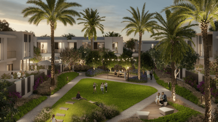 Complexe résidentiel luxueux "Talia the Valley" au crépuscule avec des bâtiments blancs modernes et une verdure luxuriante. Des palmiers bordent le chemin où les gens socialisent et profitent des coins salons extérieurs.