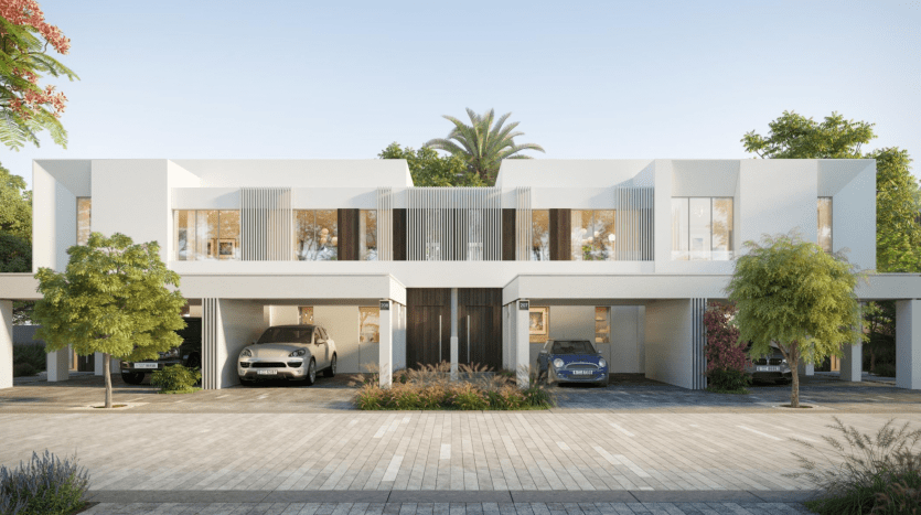 Une maison blanche moderne de deux étages à Talia the Valley, dotée de grandes fenêtres et portes en verre, entourée d'une verdure luxuriante et de palmiers, avec deux voitures garées dans un abri de voiture intégré.