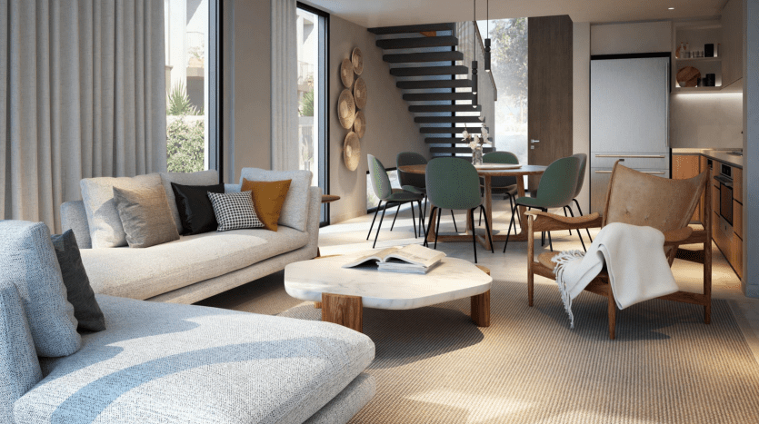 Salon moderne avec de grands canapés gris, une table basse en bois avec un livre et une chaise en cuir. Le coin repas comprend une table ronde avec des chaises vertes. Un escalier à marches flottantes mène à l'étage, tandis que de grandes fenêtres inspirées de Talia the Valley inondent l'espace de lumière naturelle.