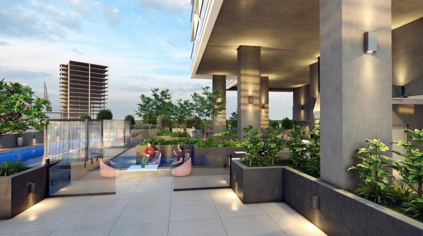 Deux personnes se prélassant au bord d'une piscine sur le toit de Catch Dubai, entourées d'une verdure luxuriante et d'une architecture moderne, avec des bâtiments et un coucher de soleil en arrière-plan.