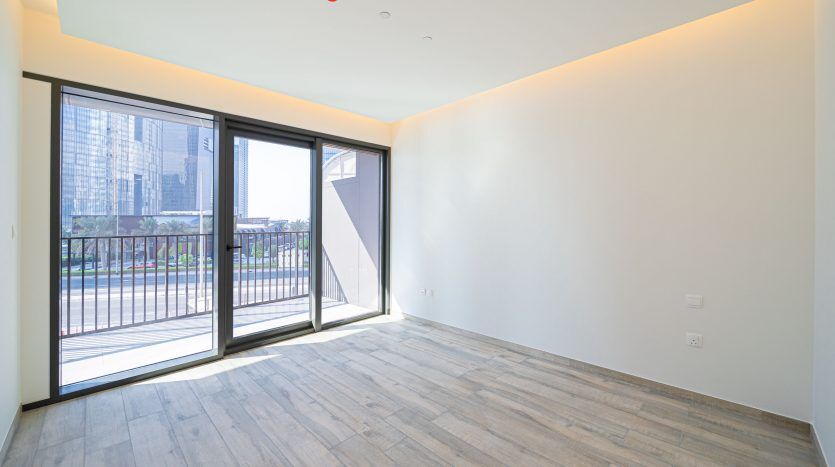 Appartement moderne et vide à Dubaï avec de grandes fenêtres donnant sur le paysage urbain, un sol en bois stratifié et des murs blancs.