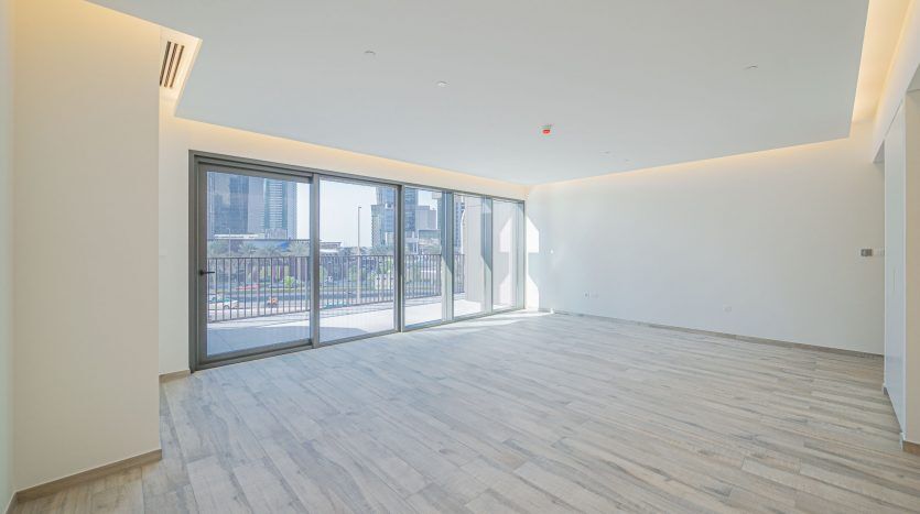 Appartement moderne et vide à Dubaï avec de grandes fenêtres, du parquet et des murs blancs, offrant une vue sur les bâtiments de la ville à l'extérieur.