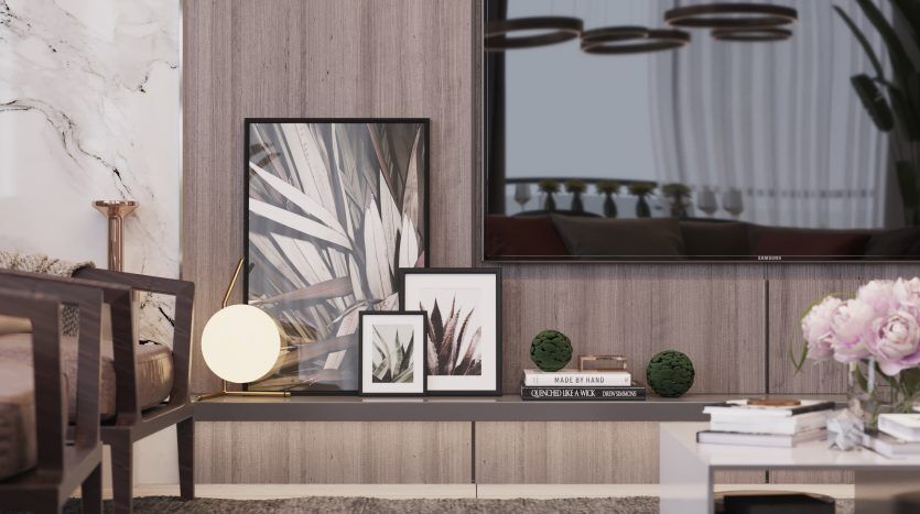 Un coin salon confortable et moderne dans un appartement de Dubaï comprenant une chaise en bois, une pile de livres et des œuvres d'art encadrées au sol contre un mur en marbre et en bois, à côté d'une fenêtre montrant un