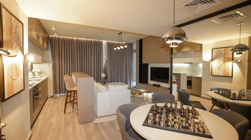 Intérieur d'appartement moderne à Dubaï comprenant un salon décloisonné avec un échiquier sur une table ronde, des sièges élégants, une kitchenette et un éclairage élégant.