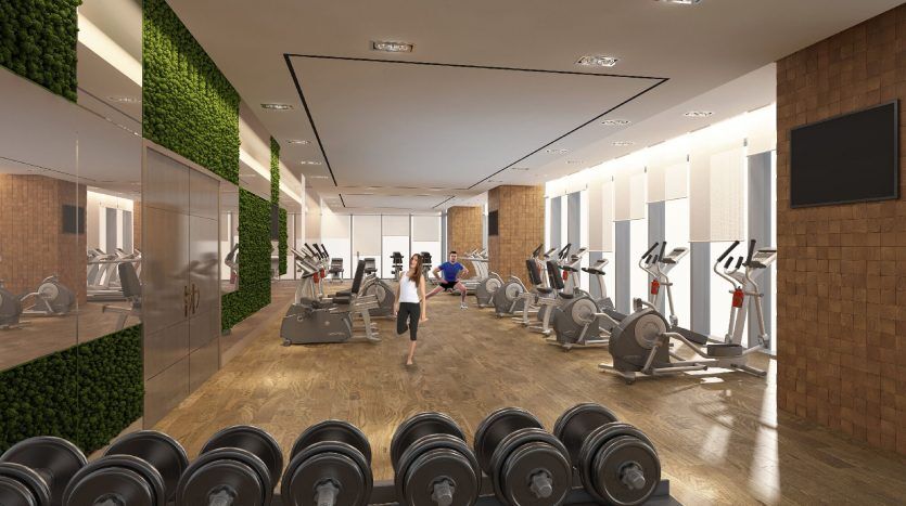 Une salle de sport spacieuse et moderne à Dubaï avec une variété d'équipements, notamment des tapis roulants, des poids et des machines elliptiques, avec des murs en miroir et des accents de bois naturel. Une personne fait du jogging sur un tapis roulant