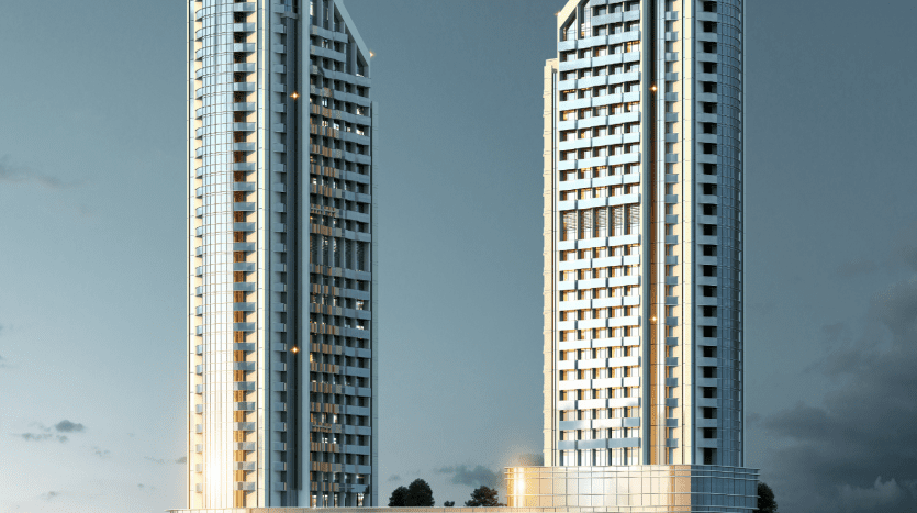 Deux immeubles modernes de grande hauteur avec des façades en verre réfléchissantes et de nombreux balcons éclairés par des lumières en début de soirée sur fond de ciel clair et d'environnements verdoyants, mettant en valeur le premier immobilier de Dubaï.