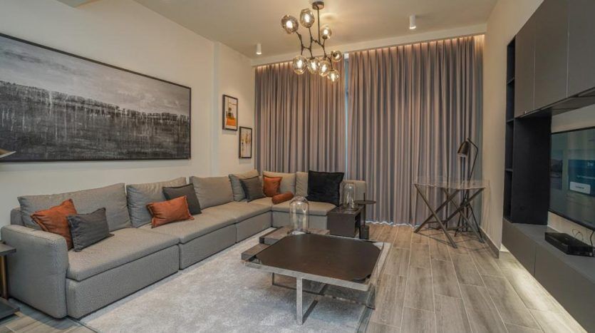 Salon moderne avec un grand canapé sectionnel gris, des coussins orange, une table basse en bois et une décoration minimaliste avec une grande œuvre d'art en noir et blanc au-dessus du canapé dans une élégante villa de Dubaï.
